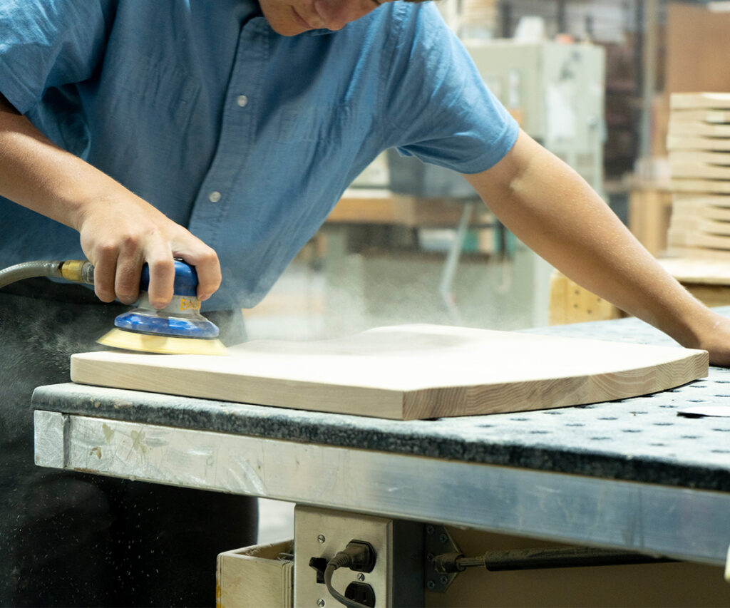 Close up of a man in a workshop sanding a board with a power sander
